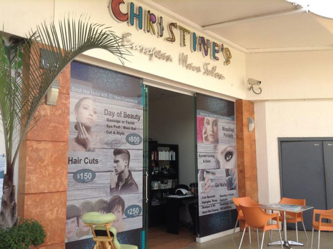 christine's hair salon storefront with posters in window advertising a variety of services a table and four chairs directly in front