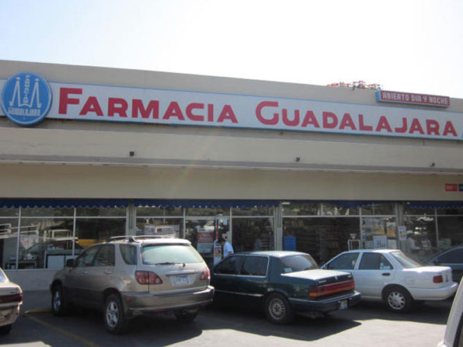 farmacia guadalajara storefront with red corporate lettering large open entranceway and cars parked out front
