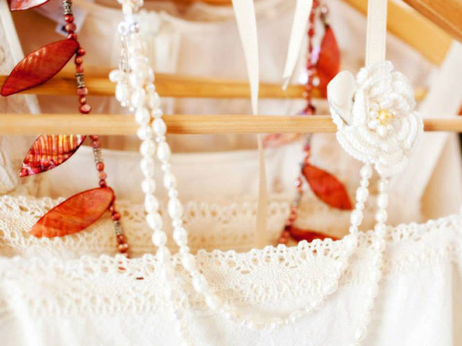 White lacy dress and white and orange beaded necklaces hanging on wooden hanger 