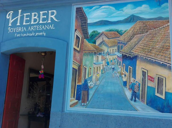 Blue store front wall with mural of typical mexican village painted beside entrance into Heber Joyeria Artesanal in Ajijic, Mexico.