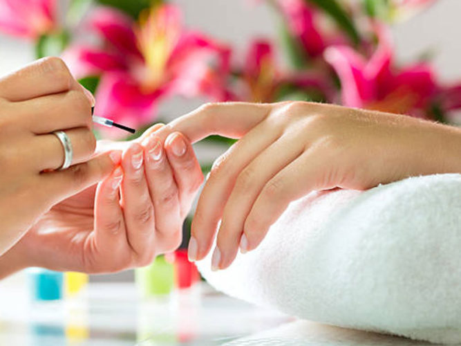 female hands painting nails of another female hand on rolled up white towel blurred image of pink lily's in background