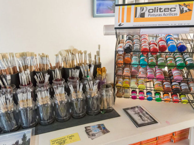 Paint brushes in jars and acrylic paints on shelves lined up for sale.