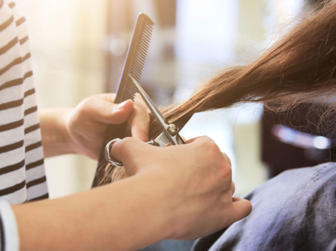 female cutting long brown hair with scissors and black comb